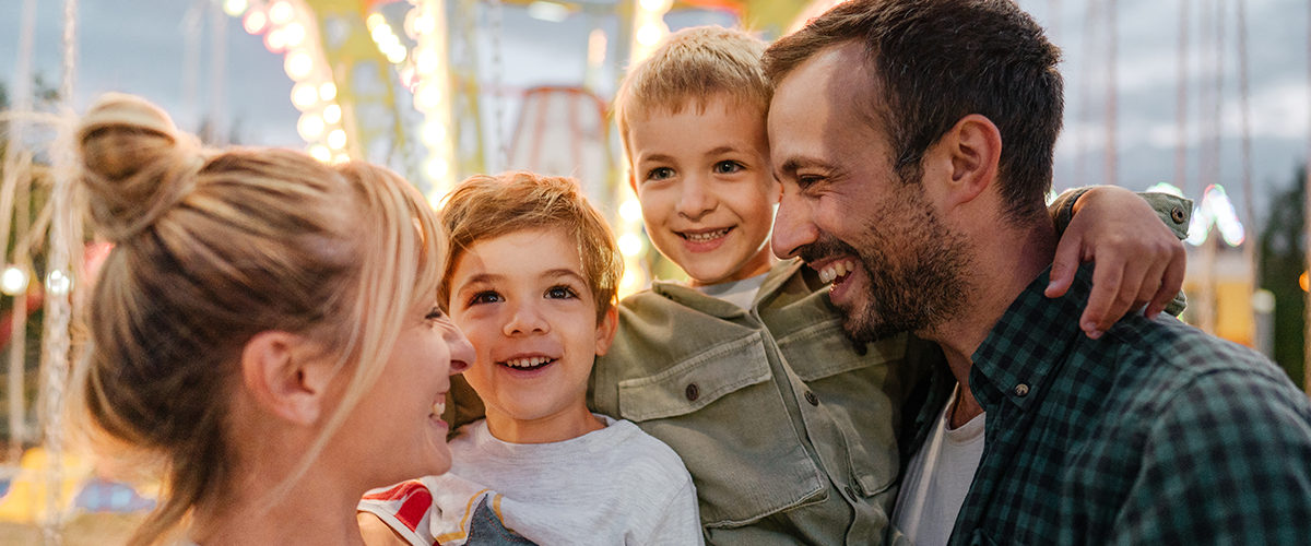 A family with two young boys, outside together at a carnival.
