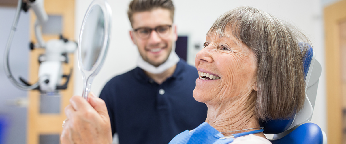 Woman looking in a handheld mirror at her teeth during a dentist appointment.