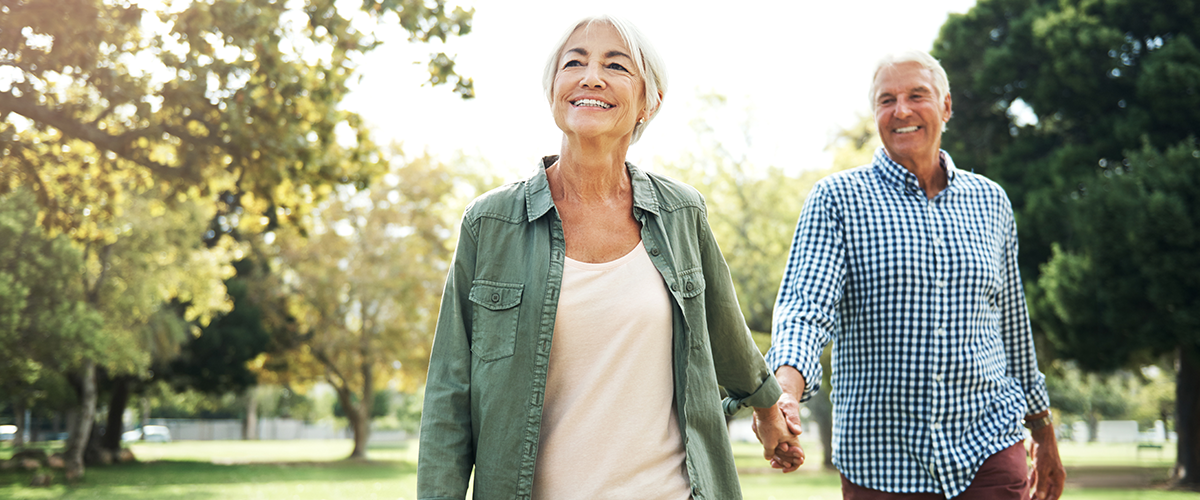 An older couple, taking a walk outside while holding hands.