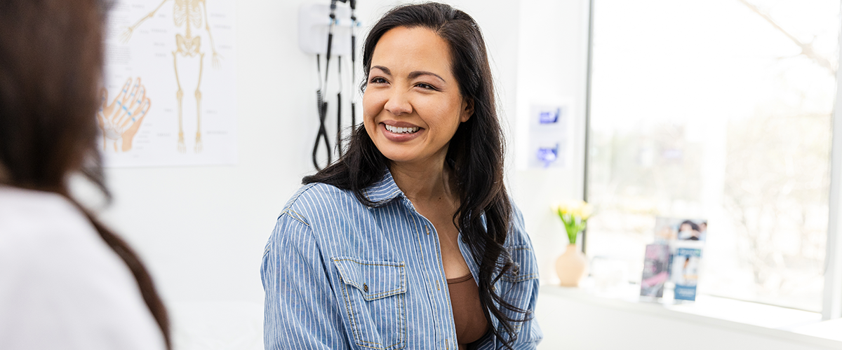 Woman sitting in a doctor's office, smiling, speaking with a physician.